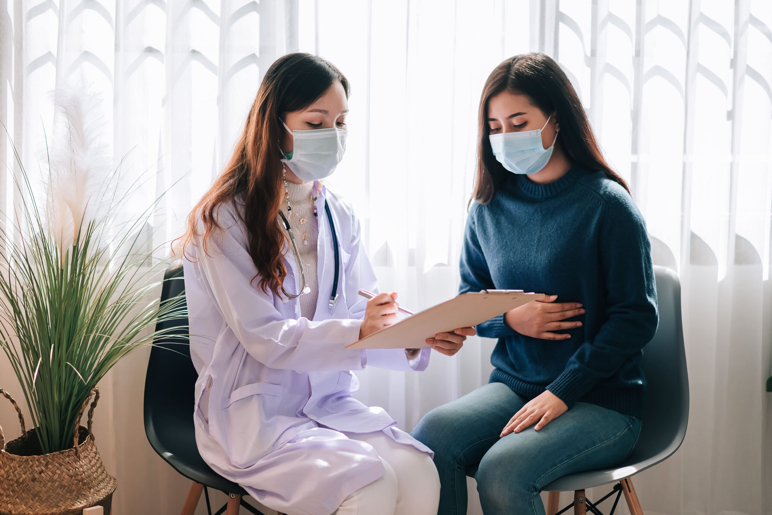 asian doctor visit examines young adult woman hospital with stomach ache doctor checking up consulting health care wearing mask protect covid19 pandemic 1 scaled